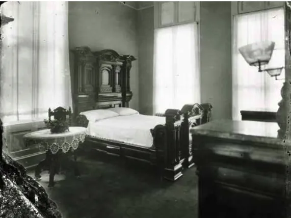 Bedroom in what was clearly one of the more upscale brothels in the "Storyville" district. Bed with large hardwood headboard and frame, small side tab, 1900